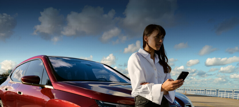 Frau ist gelehnt an BMW-Modell IX mit Fokus auf Mobiltelefon